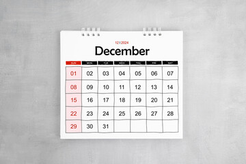 December 2024 desk calendar on gray cement wall background.