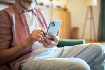 Senior man using smartphone on the couch at home
