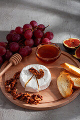 Cheese plate, still life of seasonal wine snacks. Camembert or brie cheese, grapes, walnuts, baguette, honey and figs with interesting shadows in the background. Cheese platter, appetizer on the table