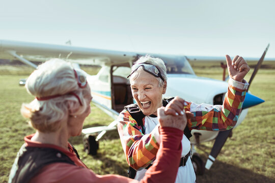 Two senior women laughing after skydiving adventure at sunset - Powered by Adobe