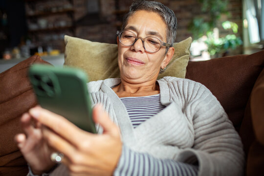 Senior woman using smartphone on cozy couch at home