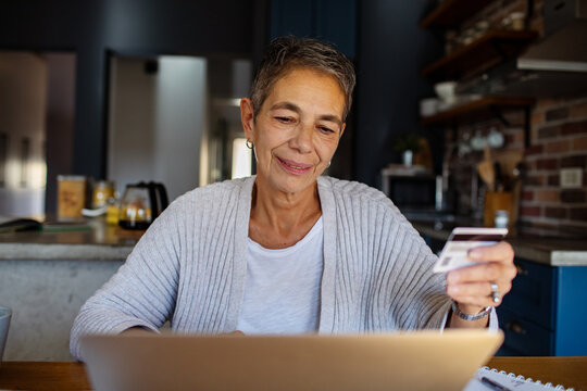 Senior woman using credit card on laptop at home