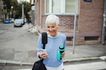 Active senior woman using smartphone while leaving gym