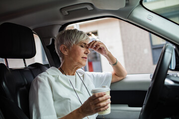 Tired senior nurse drinking coffee in her car