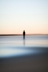 Fototapeta premium Lonely figure on beach at sunrise, soft colors