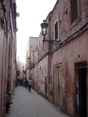  narrow, winding alley in the heart of the Moroccan medina, lined with weathered stone buildings and adorned with wrought iron lanterns.