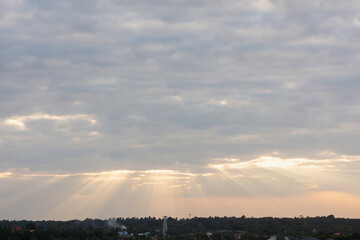 sky filled with clouds during either sunrise or sunset. Sunlight is breaking through the clouds in several places, creating a dramatic effect known as “God rays” or “crepuscular rays.”