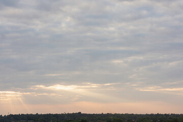 sky filled with clouds during either sunrise or sunset. Sunlight is breaking through the clouds in several places, creating a dramatic effect known as “God rays” or “crepuscular rays.”
