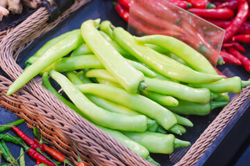 close-up of a basket filled with light green chili peppers. The peppers are elongated and smooth.there are red chili peppers and a few smaller green and red peppers scattered around.
