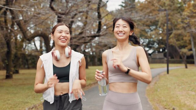 Asian women, fitness and running with water at park for workout, cardio exercise or training in nature. Active friends, japanese runner or female people with smile for health and wellness on path
