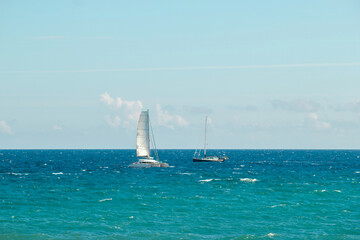 A serene view of two sailing boats gliding on the vibrant blue ocean under a clear sky.
