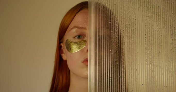 A woman with an eye patch looks at the camera with a serious look. Half of her face is covered with glass with water running down it. Studio photo