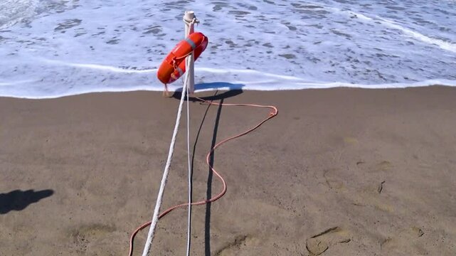 Foreshore of the sandy beach with a stake, life buoy, and rope.
