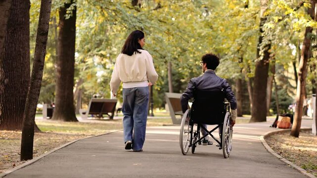 Young woman walking with her disabled friend in wheelchair in a park