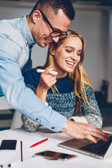 Cheerful male and female students collaborating on coursework searching information online using laptop computer, woman smiling having consultancy with coach explaining how to update application