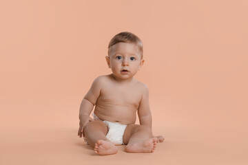 Cute little baby in diaper sitting on beige background