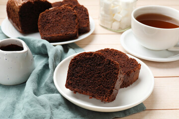 Slices of delicious chocolate sponge cake and tea on white wooden table