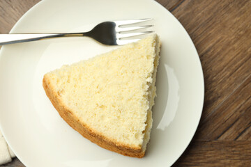 Piece of delicious sponge cake and fork on wooden table, top view