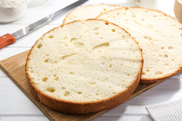 Delicious cut sponge cake and knife on white wooden table