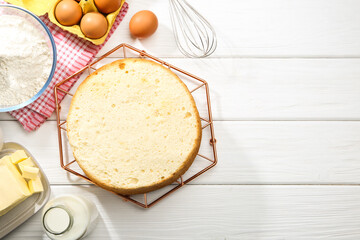 Delicious cut sponge cake and ingredients on white wooden table, flat lay. Space for text