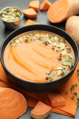 Delicious sweet potato soup with pumpkin seeds in bowl and vegetables on grey table, closeup