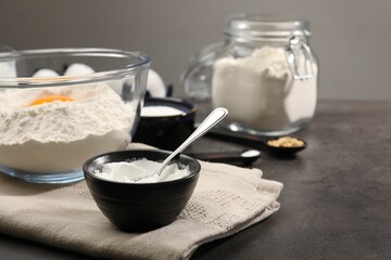 Baking powder and spoon in bowl on grey textured table, closeup
