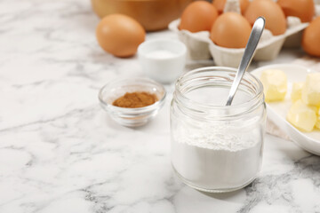 Baking powder in jar and other products on white marble table, closeup. Space for text