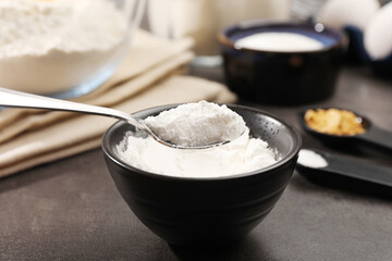 Taking baking powder from bowl with spoon at grey textured table, closeup