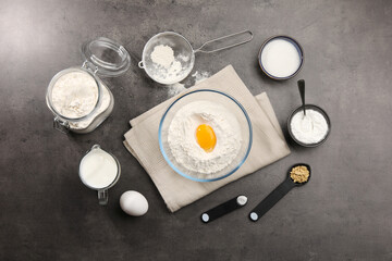Baking powder with egg yolk in bowl surrounded by other products on grey textured table, flat lay