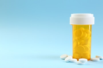 Bottle of antibiotic pills on light blue background, space for text