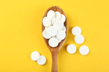 Antibiotic pills in spoon on yellow background, top view