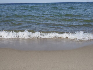 Calm sea shore with sandy beach and waves rolling onto the shore under clear sky
