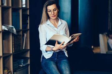 Cropped image of young beautiful serious woman reading articles in magazine holding in hands during...
