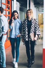 Fototapeta premium Attractive cheerful woman talking with man colleague during downloading application on smartphone connected to internet while hipster girls passing along and communicating using modern cellular