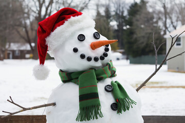 The snowman is wearing a red Santa hat, a green scarf, and has coal black buttons for eyes