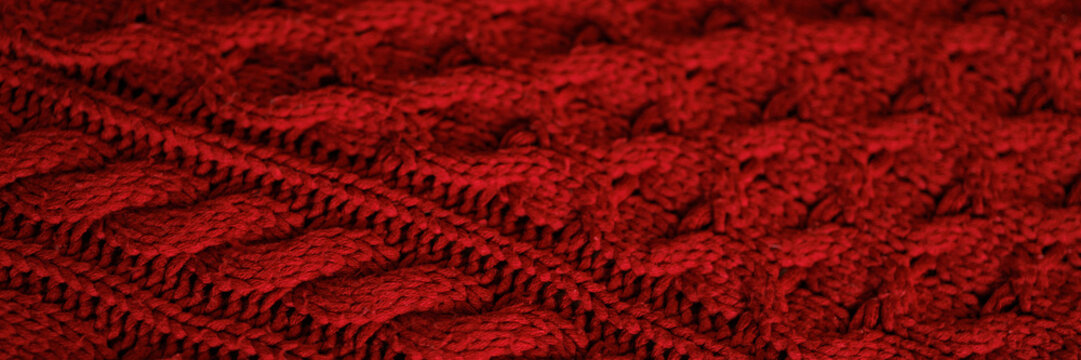 A close up of a red knit sweater. The sweater is red and has a pattern of squares and triangles. Banner with copy space.