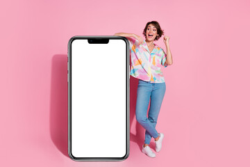 Full body portrait of nice young woman raise fist empty space smart phone display isolated on pink...