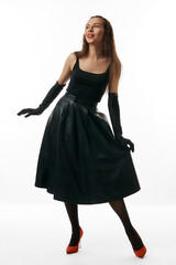 beautiful girl in black dress, gloves and red shoes poses in studio on white background