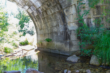 A serene stream flows beneath the Puente del Perdón, surrounded by lush greenery in Sierra de...