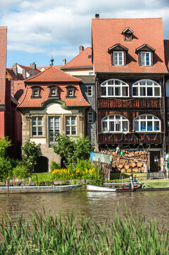 Historische H&auml;userfront mit Holzveranda, Bogenfenstern und Sprossenfenstern und Brennholzvorrat an Fluss Regnitz mit Booten in Klein Venedig in der Inselstadt in Bamberg 