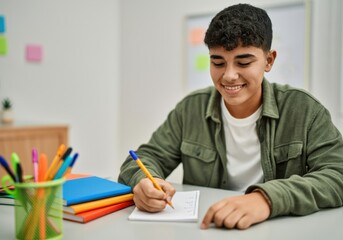 Young hispanic student smiling confident writing on notebook at classroom