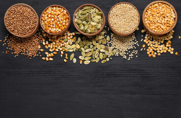 Different types of seeds and cereals in bowls on black wooden table, flat lay. Space for text