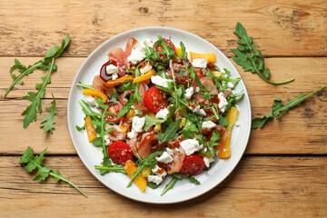 Tasty salad with arugula, cheese and vegetables on wooden table, flat lay
