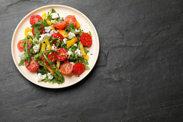 Tasty salad with arugula, cheese and vegetables on dark textured table, top view. Space for text