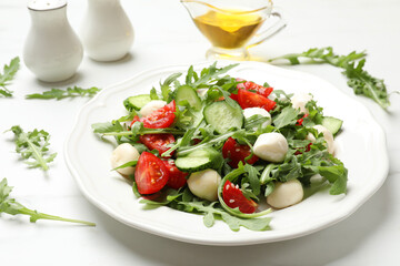 Tasty salad with arugula, mozzarella, tomatoes and cucumber on white table, closeup