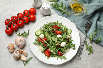 Tasty salad with arugula, mozzarella, tomatoes and cucumber served on grey textured table, flat lay
