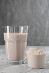 Delicious protein shake in glass and scoop with powder on grey table