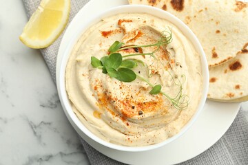 Delicious hummus with paprika, pita and lemon on white marble table, top view