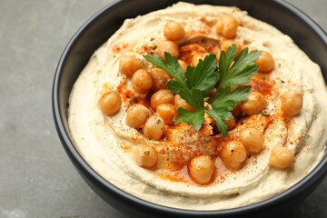 Delicious hummus with parsley, paprika and chickpeas in bowl on grey table, closeup