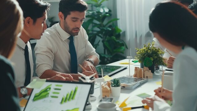 Professional smart business team discussing about using clean energy and sustainable investment at meeting table with wind mill, document with environmental graph and wooden house model. Alimentation.